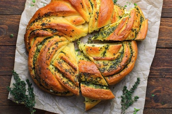 A braided bread with herbs on a wooden table.