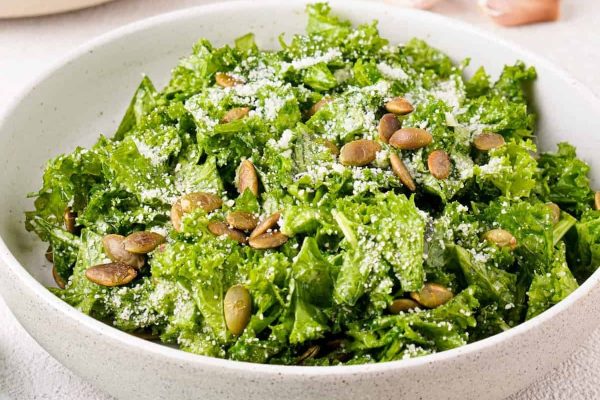 A bowl of kale salad with parmesan and pine nuts.