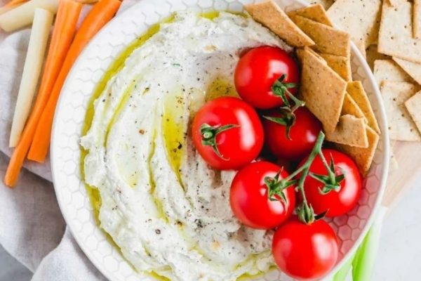 A bowl of hummus with crackers and tomatoes.