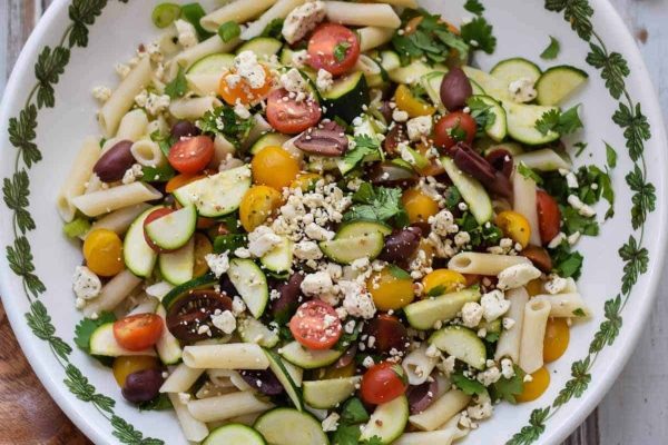 A bowl of pasta salad with tomatoes, cucumbers and feta cheese.