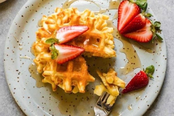 A festive Christmas breakfast recipe featuring waffles topped with fresh strawberries and drizzled with syrup on a plate.