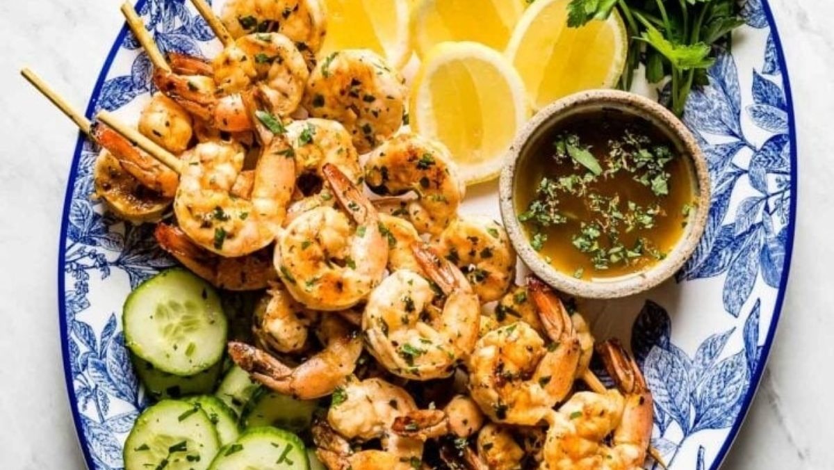 Shrimp skewers on a plate with lemons and cucumbers.