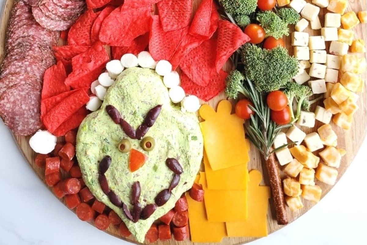 A festive platter featuring a variety of delicious cheese, meat, and vegetable recipes adorned with a whimsical grinch.