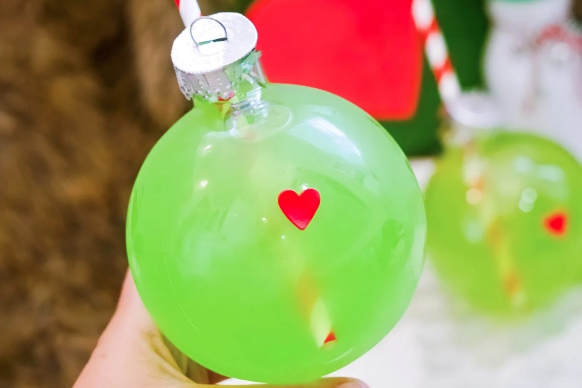 A person is holding a green balloon with a heart on it while attending a Grinch-themed party.