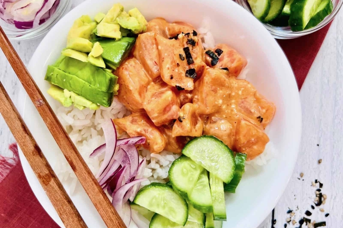 A bowl of asian food with salmon, vegetables, and chopsticks.