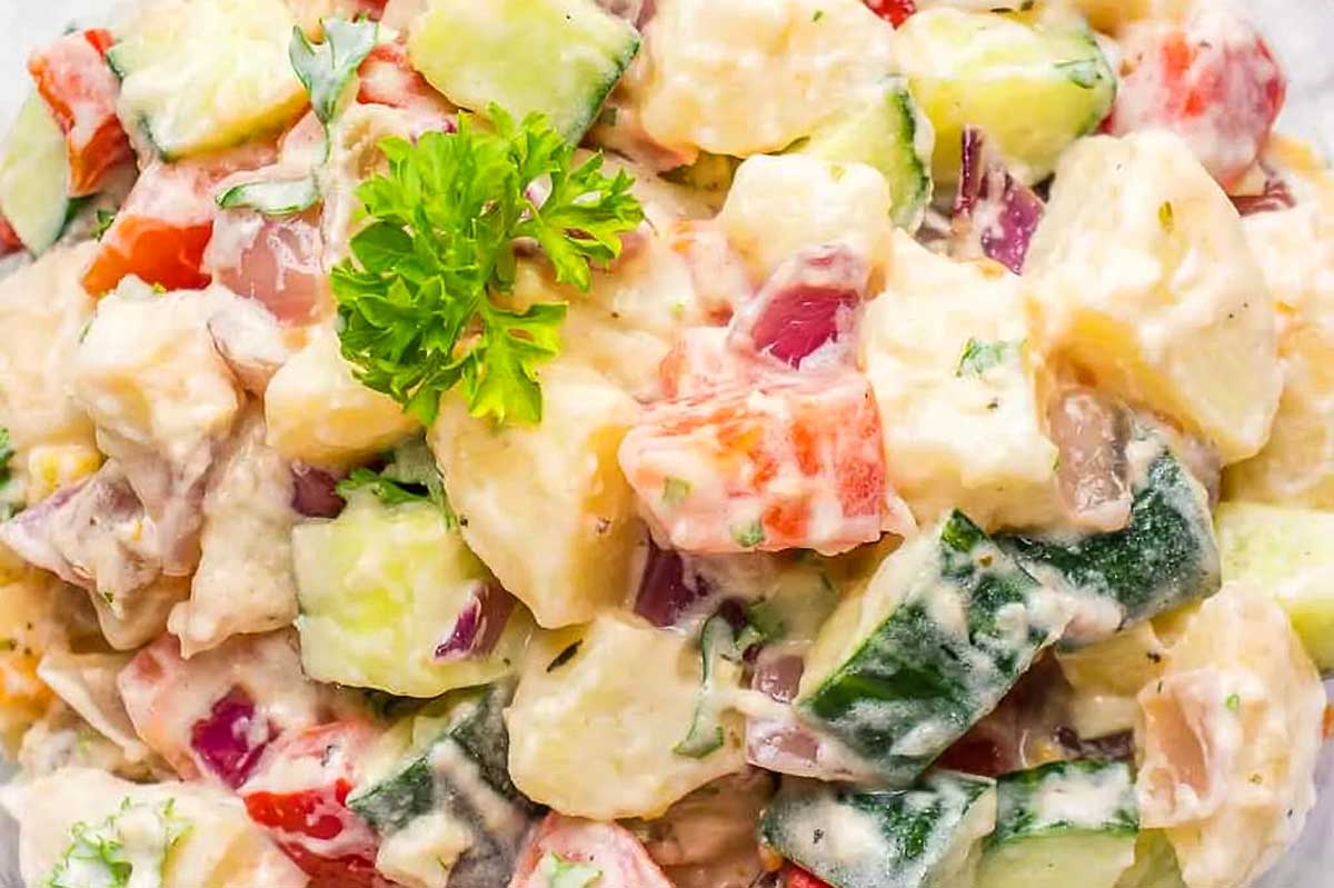 A bowl of potato salad with tomatoes and cucumbers.