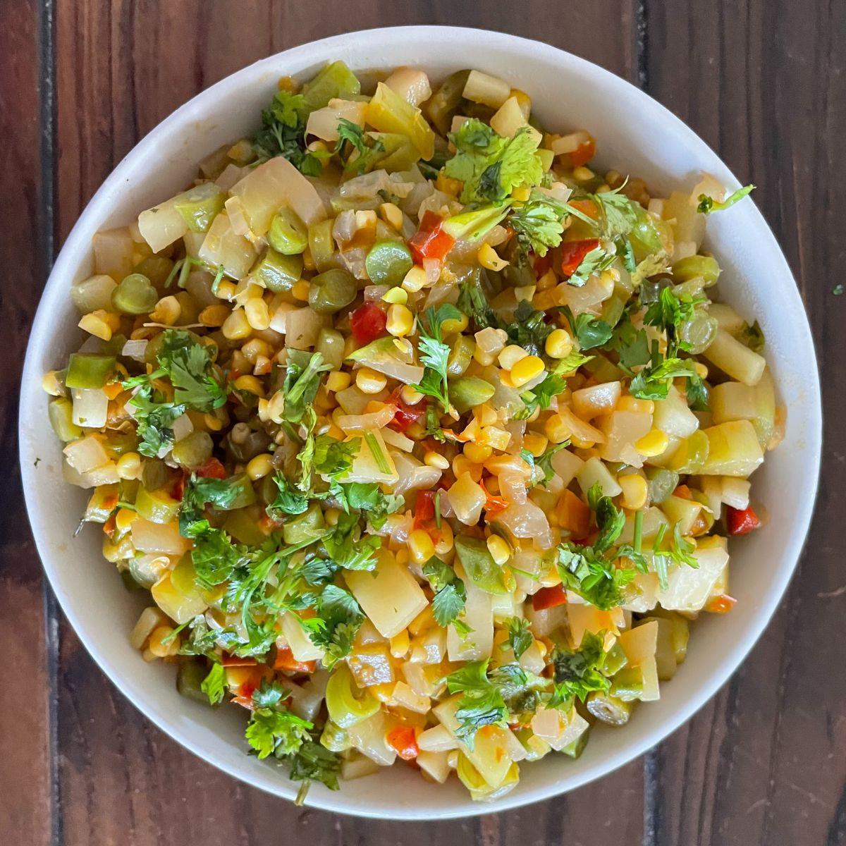 A bowl of corn and vegetable salad on a wooden table.