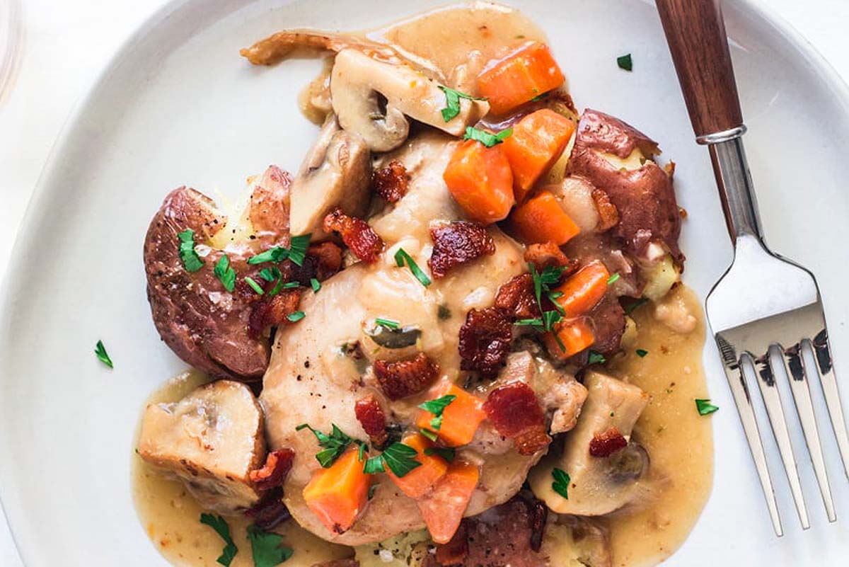 A white plate with mushrooms, carrots, potatoes and gravy.