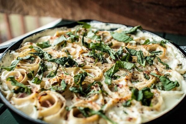 A skillet filled with pasta and spinach on a wooden table.