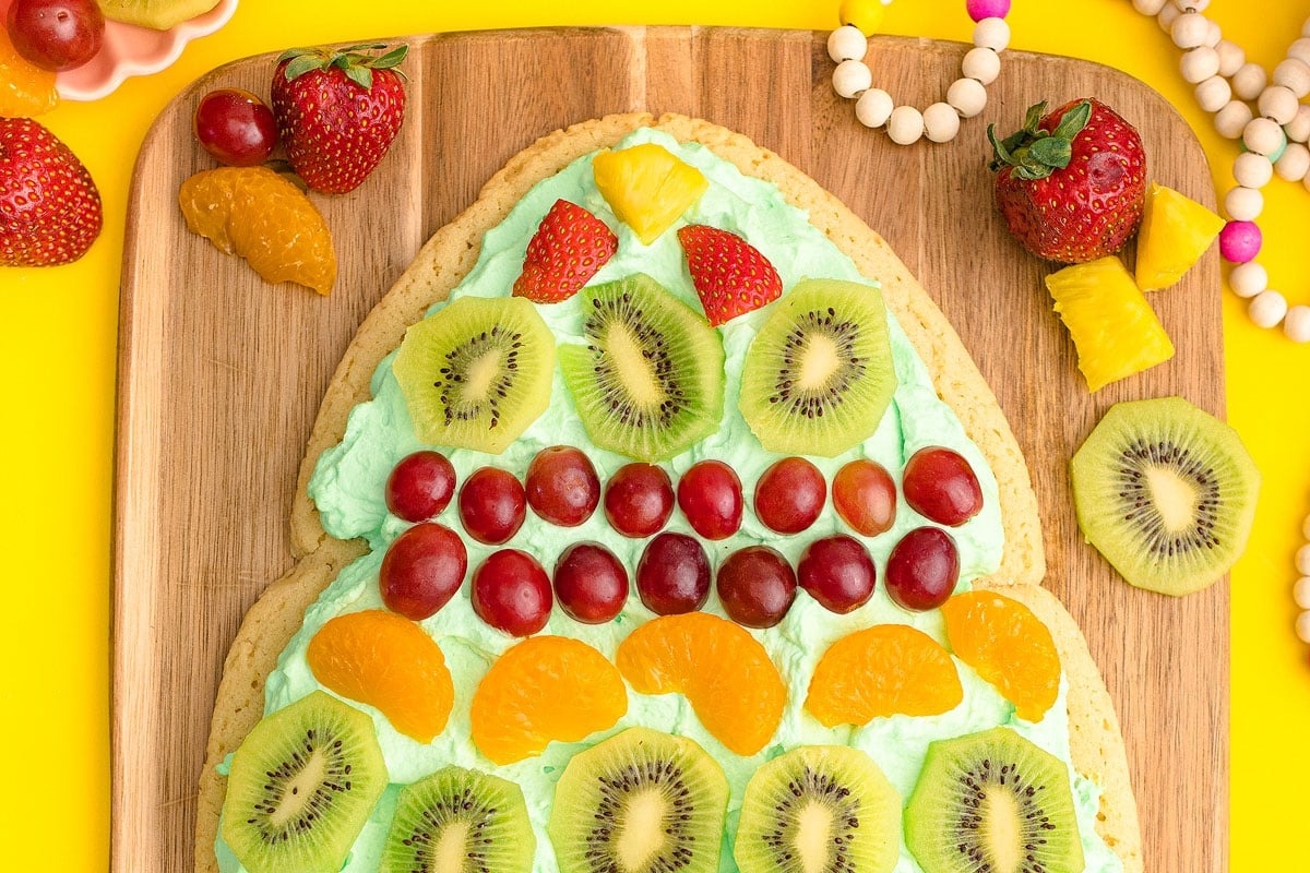 A festive Christmas cookie shaped like a fruit tree displayed on a cutting board.