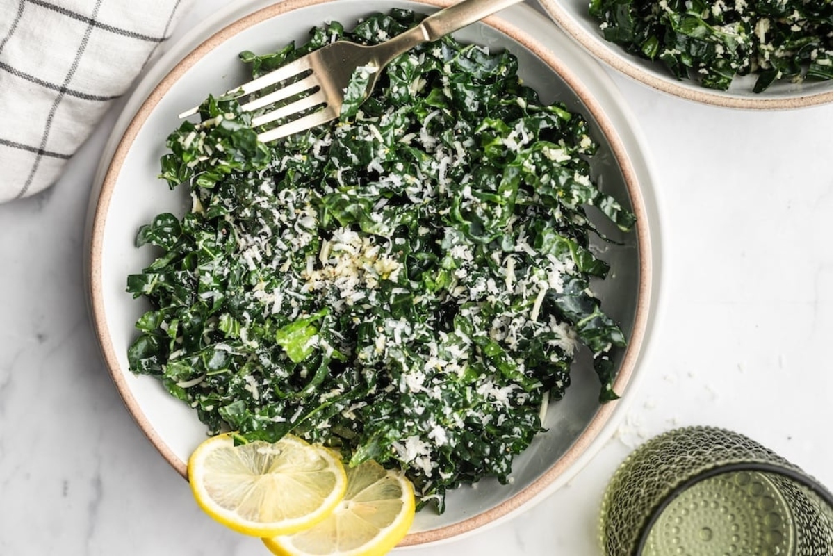 A bowl of kale salad with lemon wedges and parmesan cheese, perfect as a side dish.