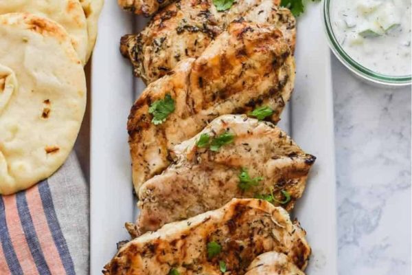 Grilled chicken on a white plate with pita bread and tzatziki sauce for a savory grilling experience.