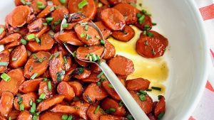 Roasted carrots in a white bowl with a spoon, perfect for your Thanksgiving feast or potluck gathering. Plus, this cheap and delicious side dish is sure to please everyone!