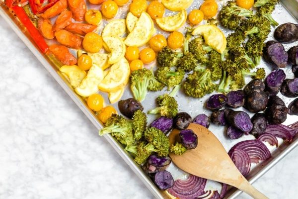 Rainbow roasted vegetables on a baking sheet with a wooden spoon.