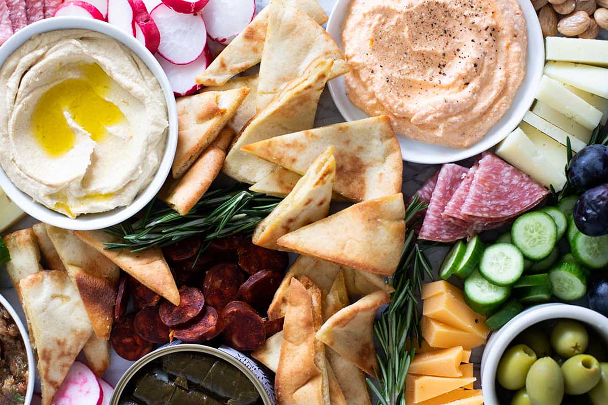 A platter of hummus, pita chips, olives and dips.