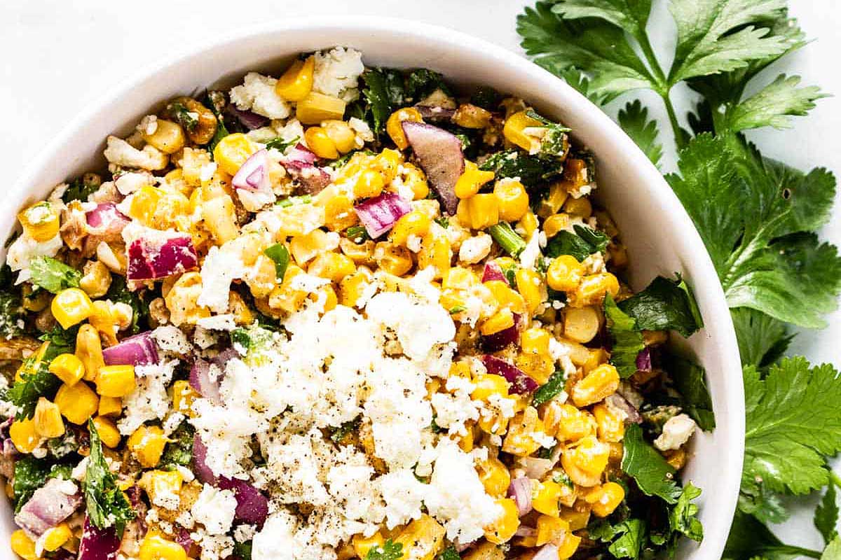A bowl of corn salad with parsley and feta cheese.