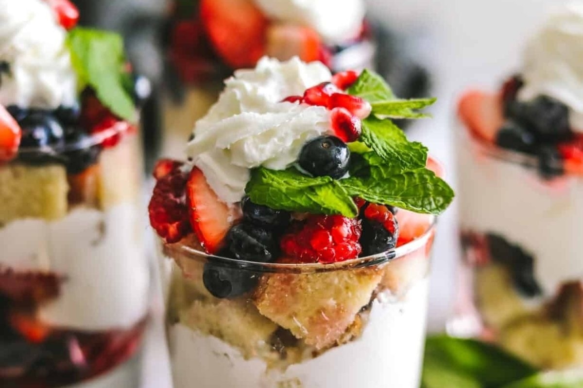 A berry trifle in a glass with whipped cream and berries, perfect for indulging in trifles.