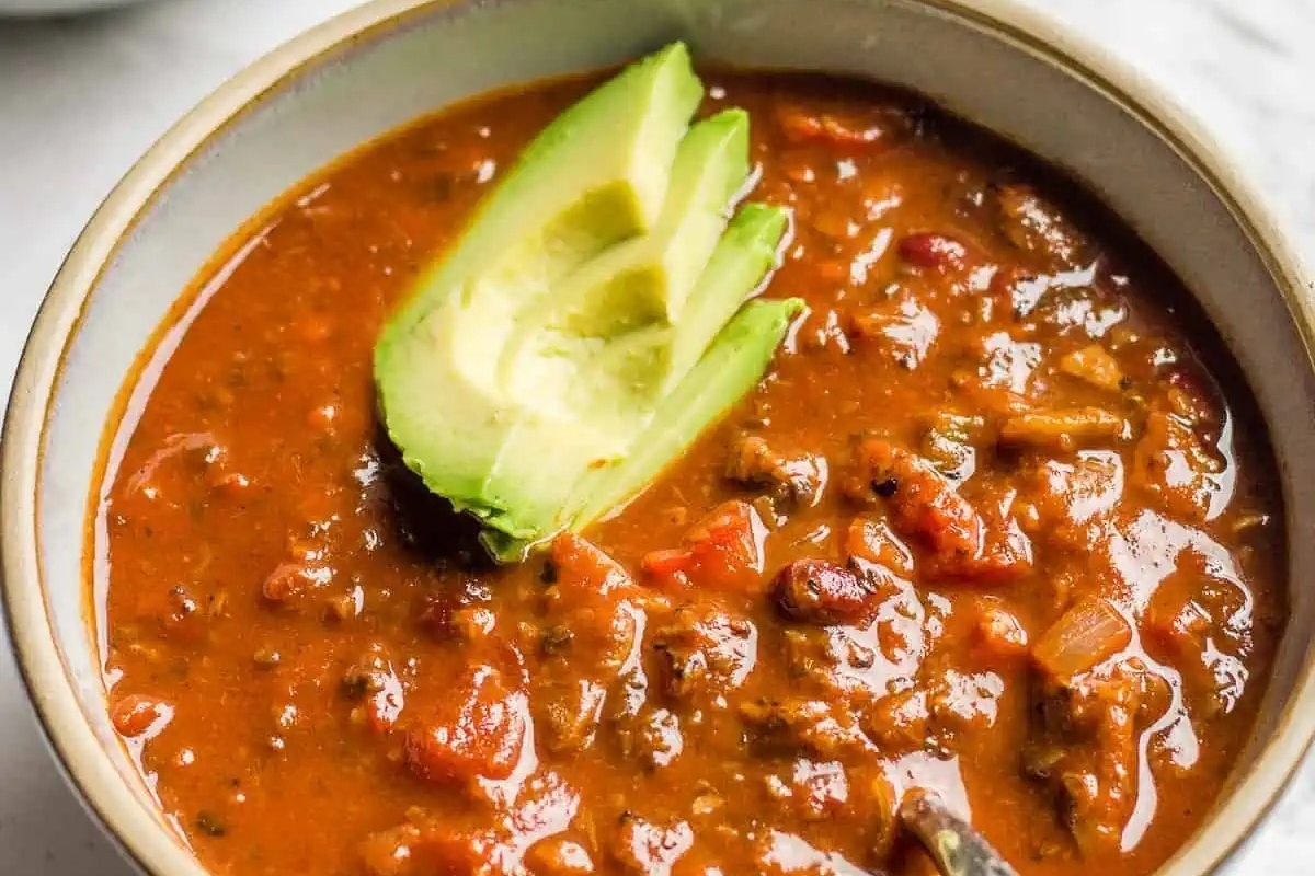 A bowl of chili with avocado and tomatoes, perfect for those looking for delicious recipes that are packed with flavor.