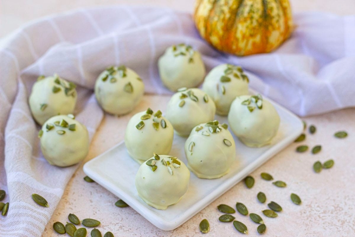 White pumpkin truffles on a white plate with pumpkin seeds are a delightful holiday treat.
