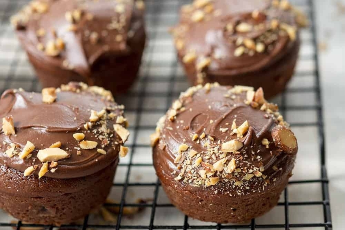 Four chocolate muffins with nuts on a cooling rack.