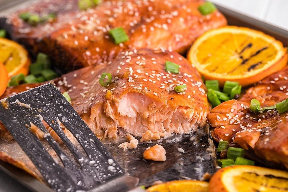 Salmon with orange slices and sesame seeds on a baking sheet.
