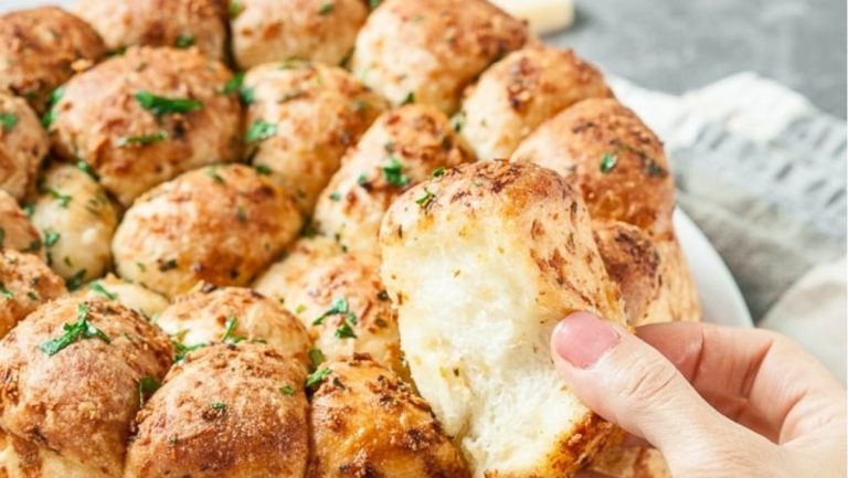 A person taking a bite out of a cheesy bread.