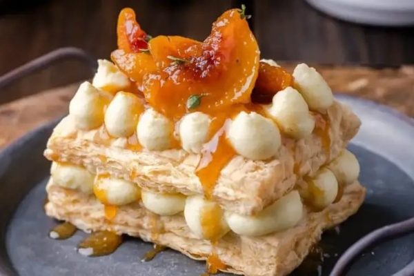 A stack of pastries with apricots and cream on a plate.