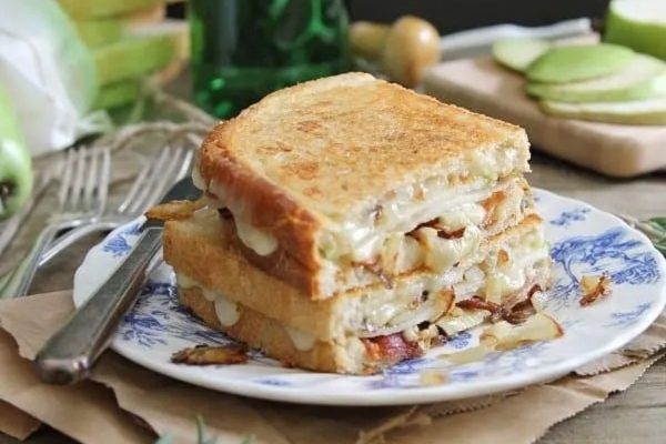 A stack of grilled cheese with apples on a plate.