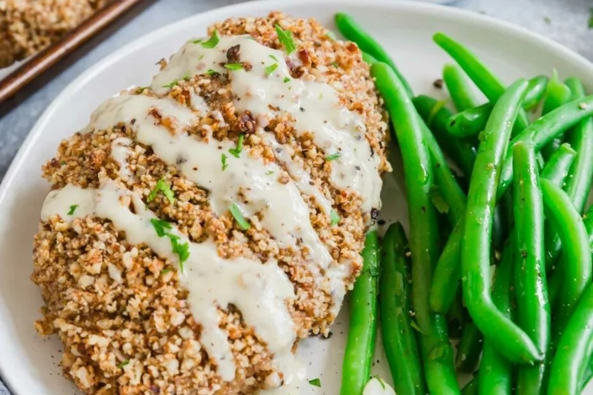 A plate with chicken breasts and green beans on it, drizzled with a pecan sauce.