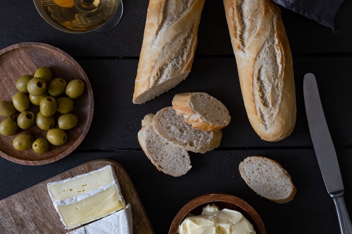 Bread, olives, cheese, and olive oil are beautifully arranged on a wooden board.