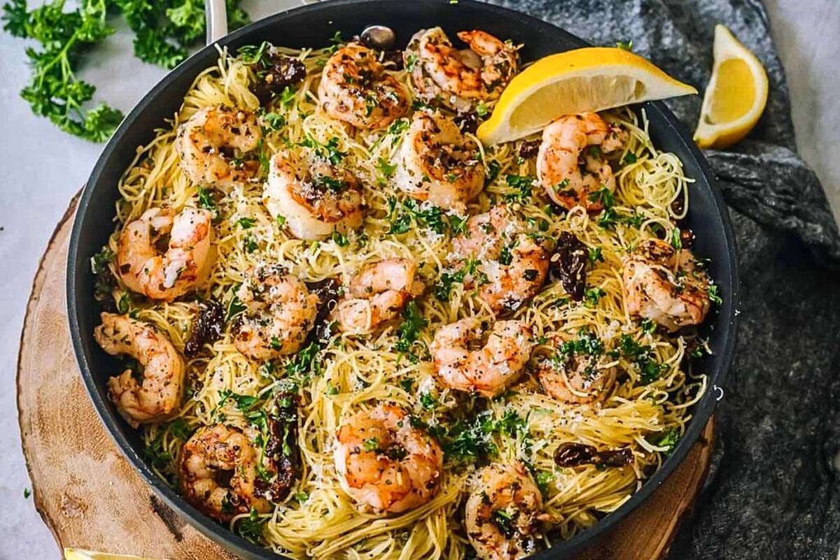 Shrimp pasta in a skillet with lemon wedges and pesto sauce.