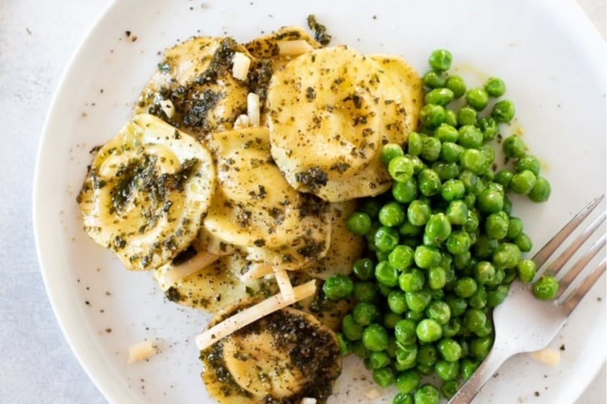 Cheesy spinach ravioli with peas and pesto on a white plate.