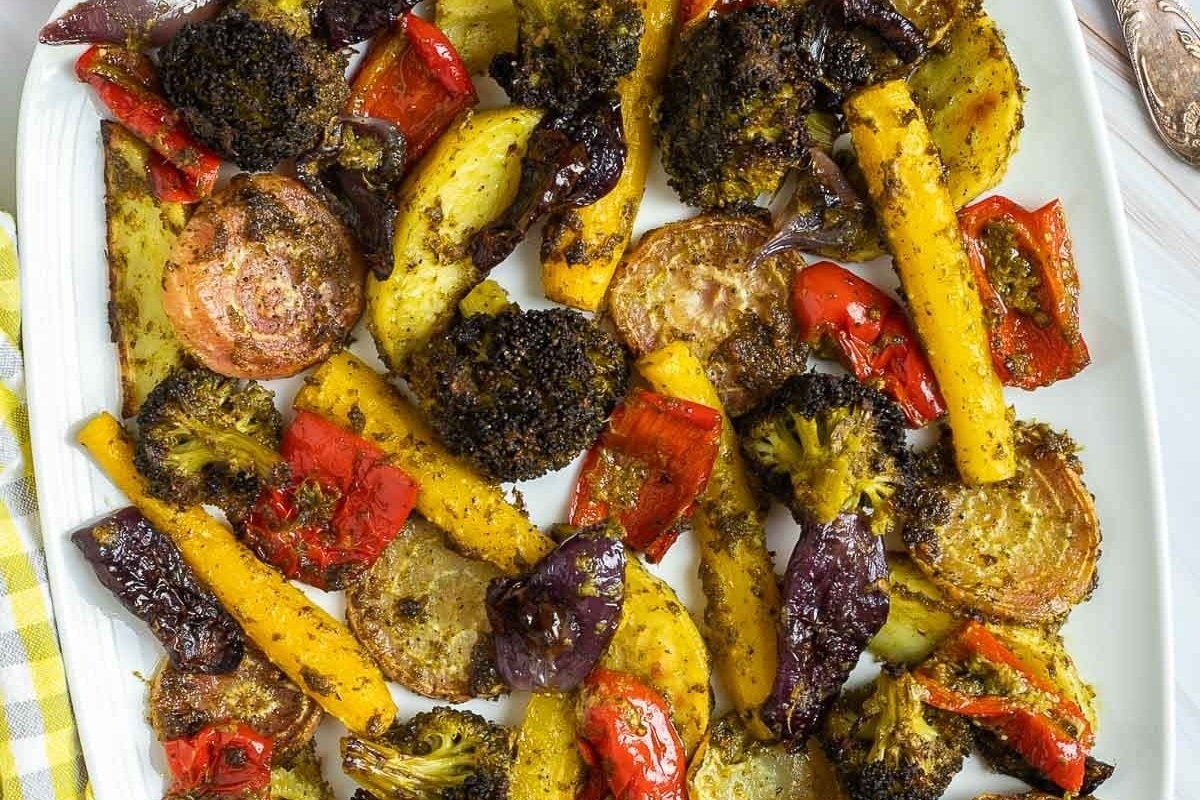 Roasted vegetables on a white plate with a fork, drizzled with pesto.