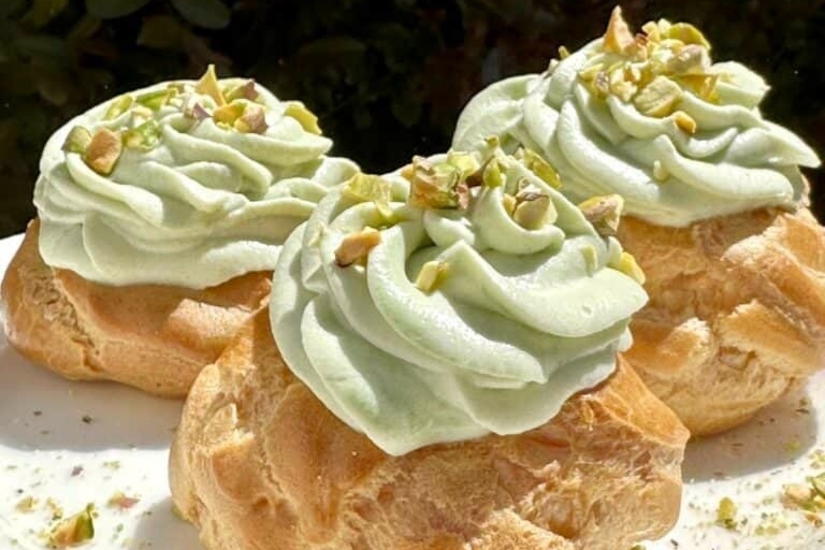 Three pastries with green icing and pistachios on a plate, perfect for pistachio lovers.
