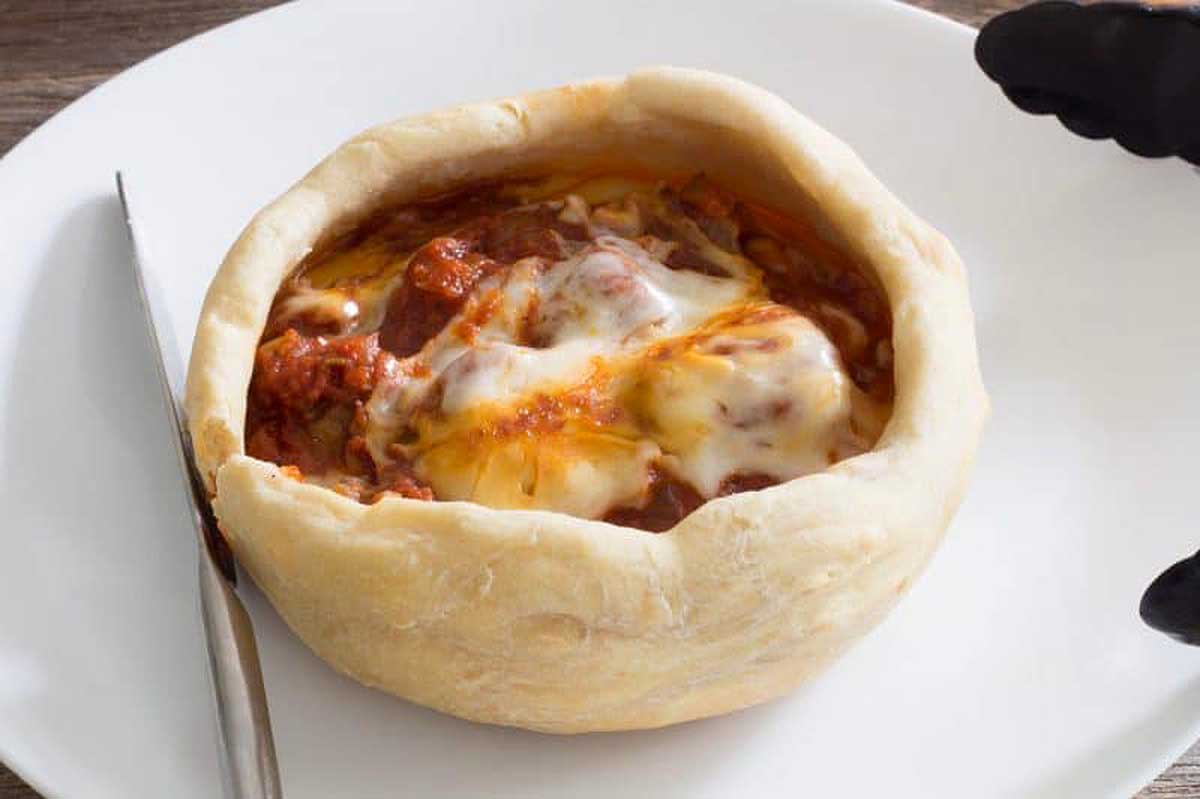 A pizza in a bread bowl on a plate.