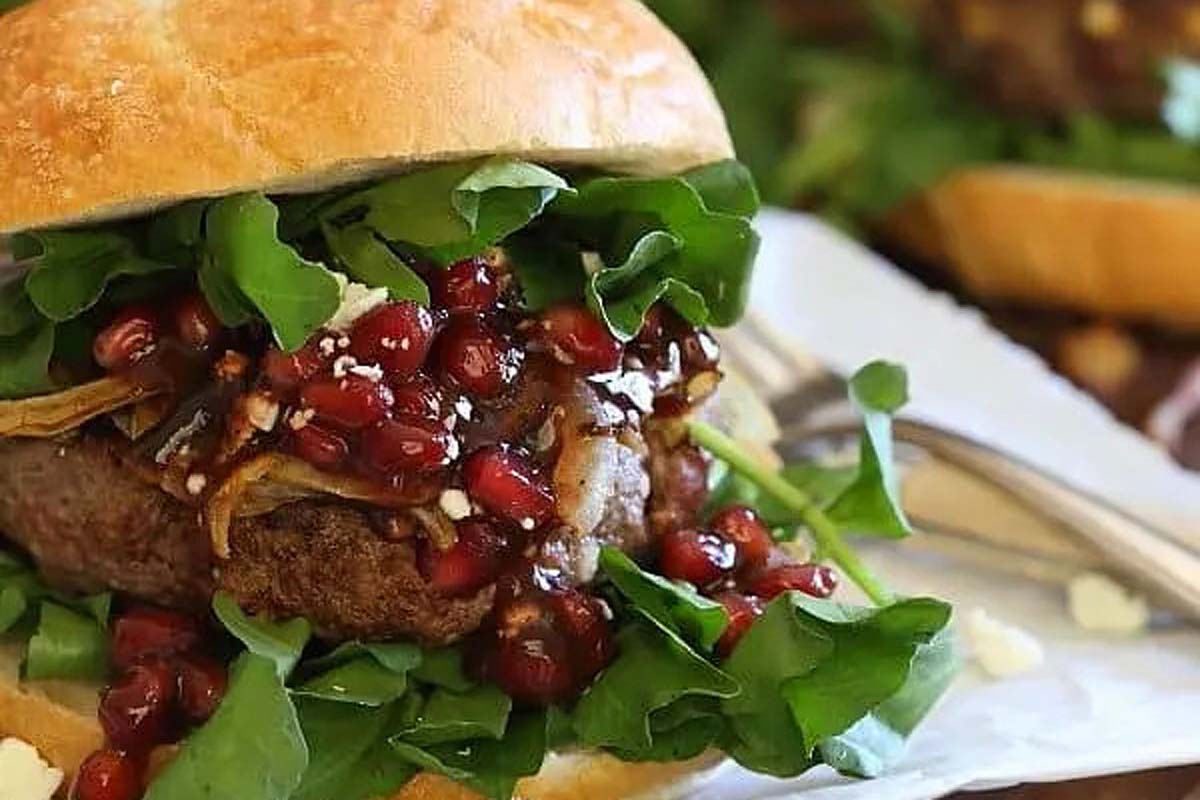 A burger with pomegranate and greens on it.