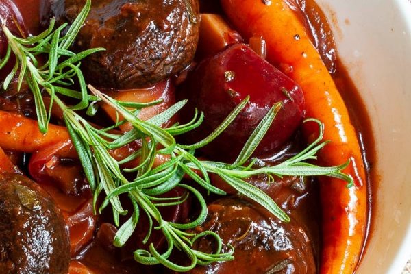 A bowl of stew with meatballs, carrots and sprigs of rosemary.