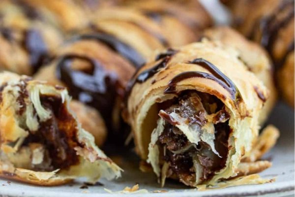 A plate of chocolate croissants with a bite taken out of them.