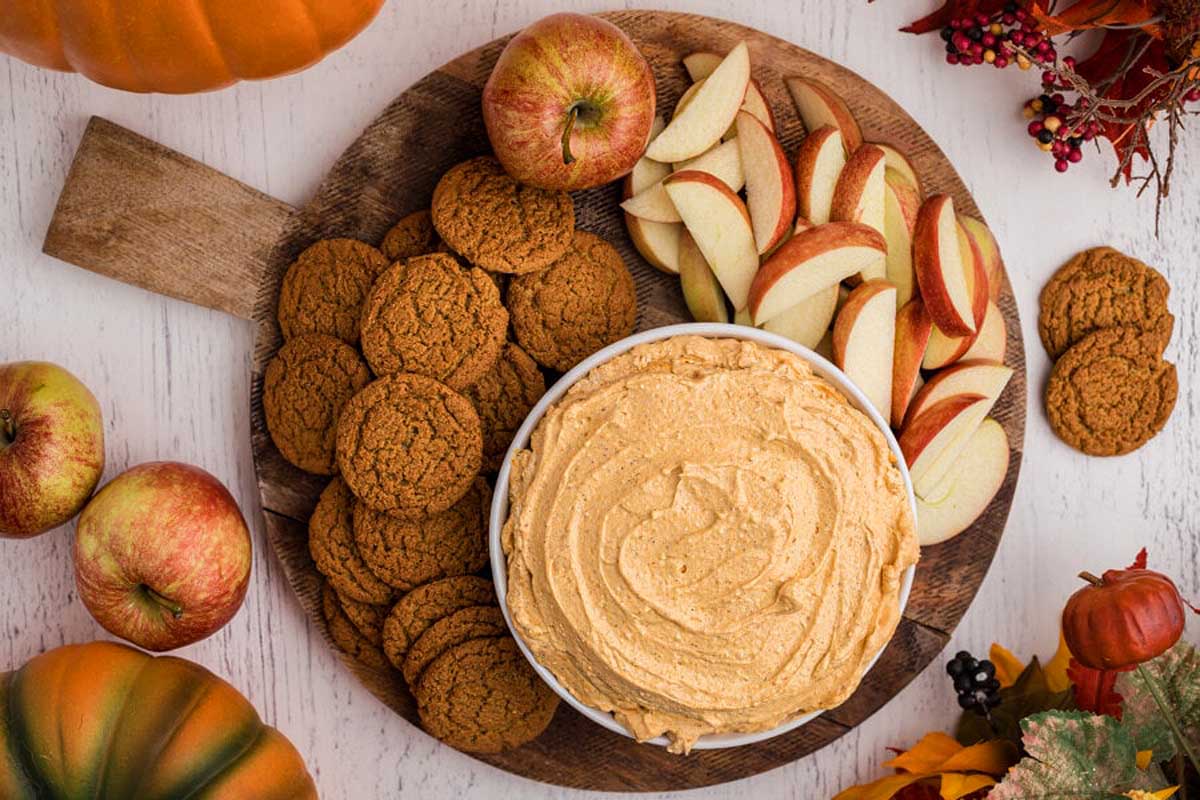 A plate with a pumpkin dip, apples, and cookies.