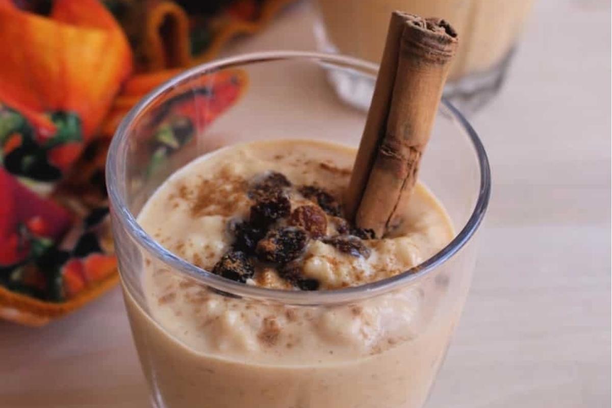 A holiday-inspired glass of pumpkin spice smoothie with cinnamon sticks.