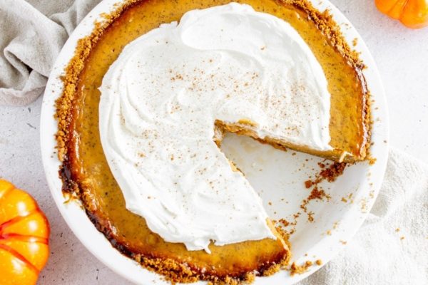 A pumpkin pie with whipped cream and a slice taken out.