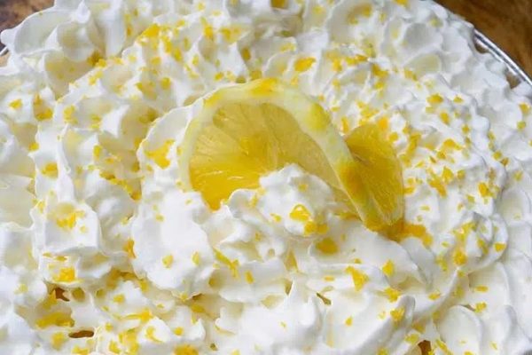 A lemon pie with whipped cream and a slice of lemon.