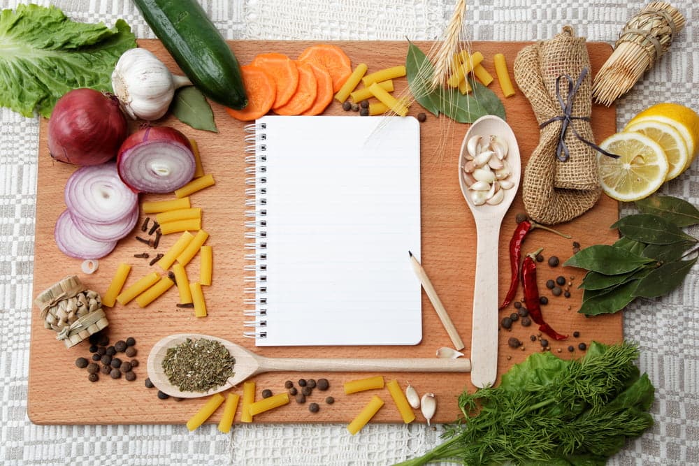 A notepad with vegetables and herbs on a wooden cutting board.