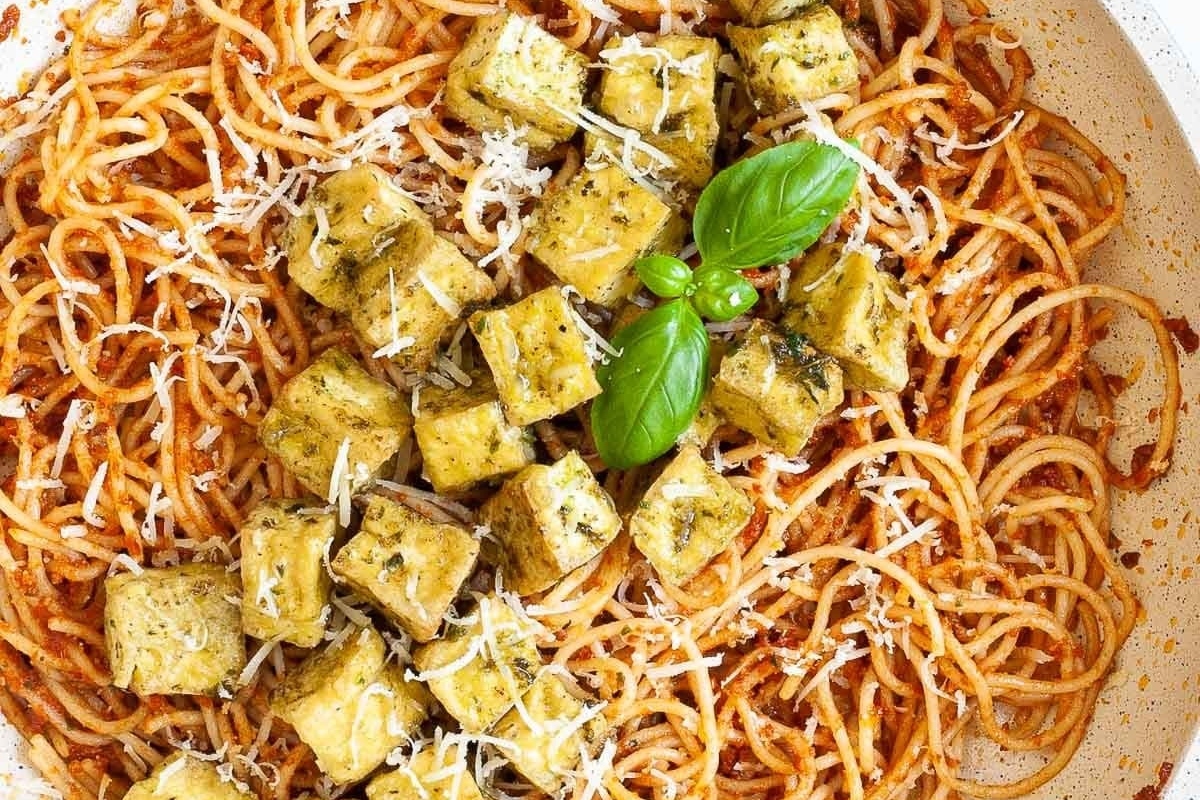 A bowl of spaghetti with tofu and basil in a pesto sauce.