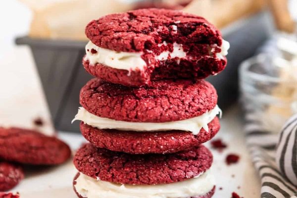 A stack of luscious red velvet cookies delicately frosted with cream cheese goodness.