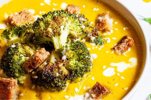 A creamy bowl of soup with broccoli and croutons.