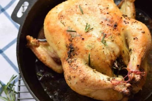 Roasted chicken in a cast iron skillet with rosemary sprigs.