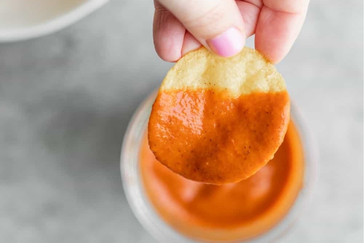 A person holding a chip with sauce on it.
