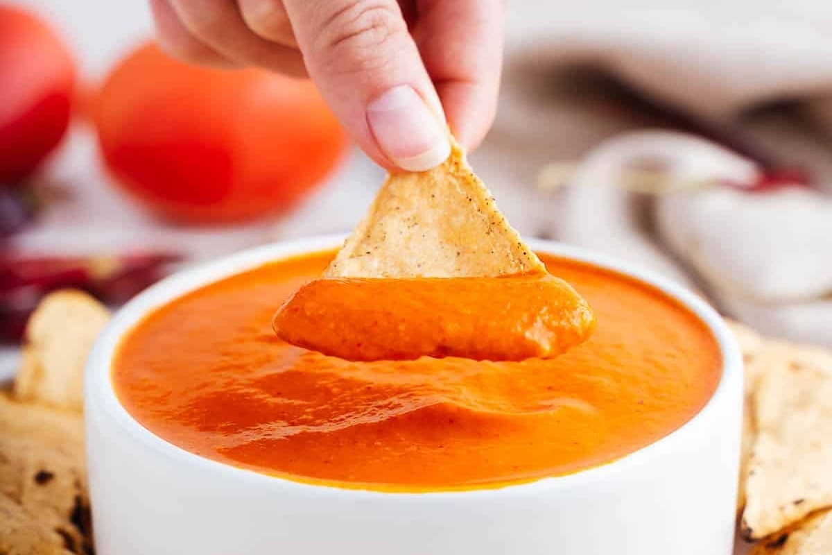 A person dipping a tortilla chip into a bowl of tomato dip.