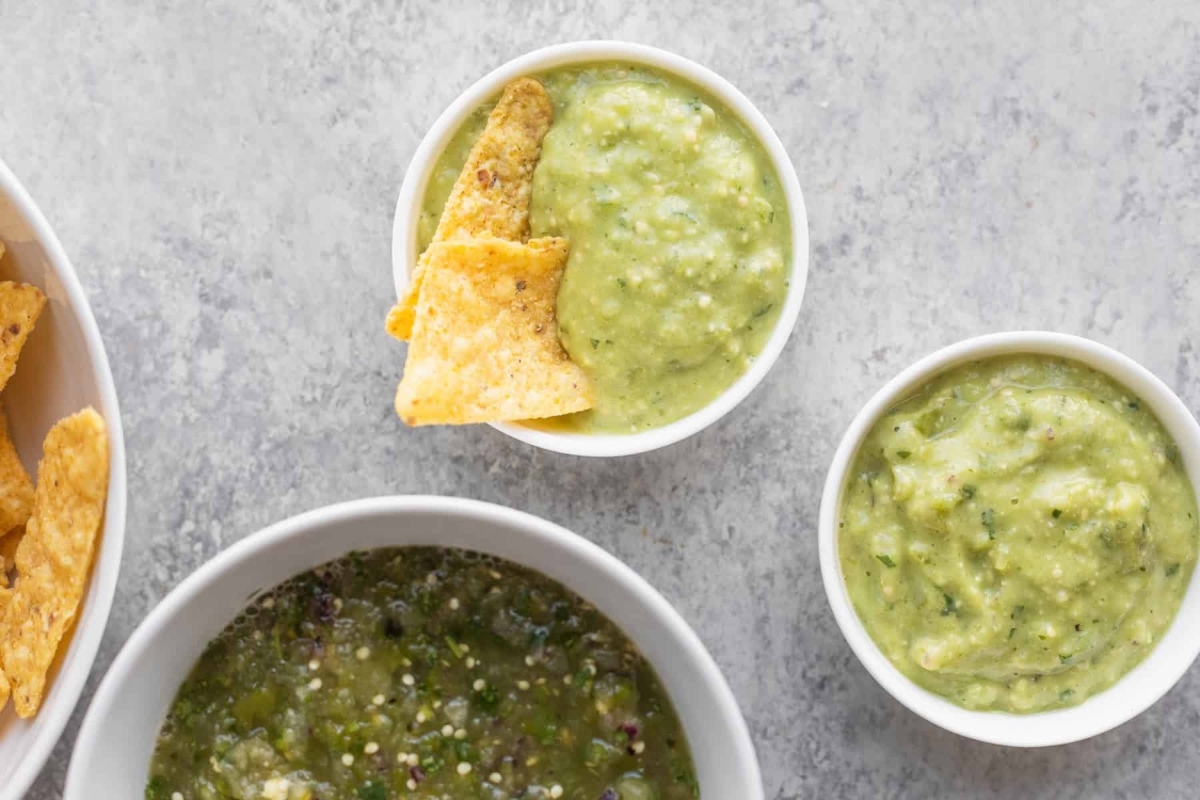 Three bowls of green salsa and tortilla chips.